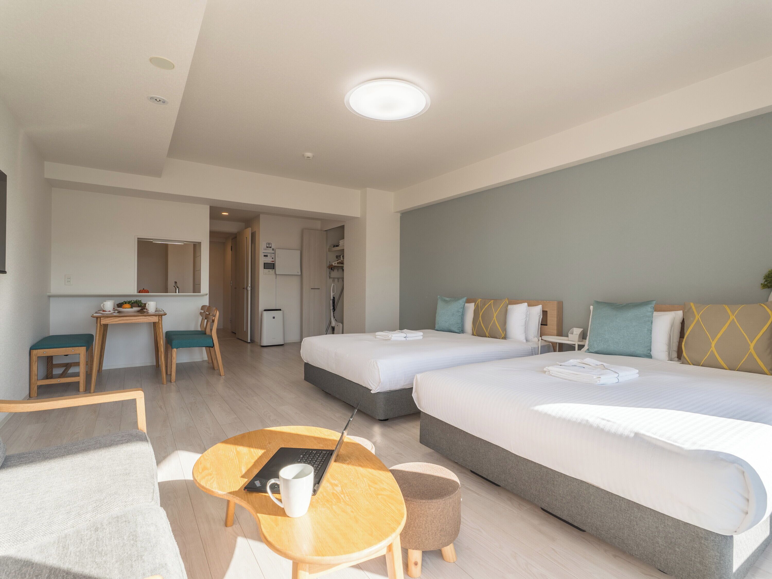 A hotel room with two beds, a small table with a laptop, a chair, and a sofa.