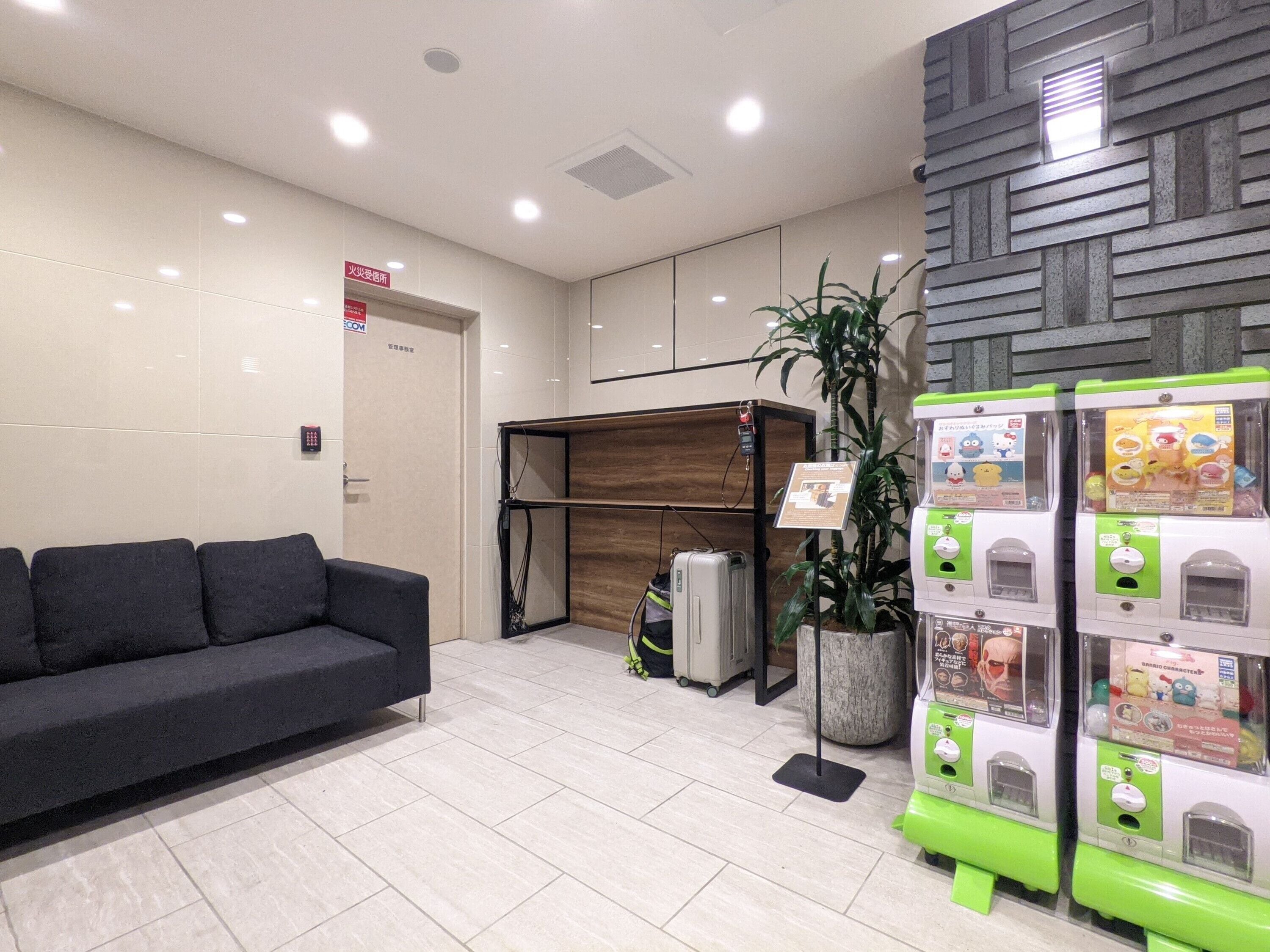 A modern lobby with a reception desk, a black sofa, a vending machine, and a potted plant.