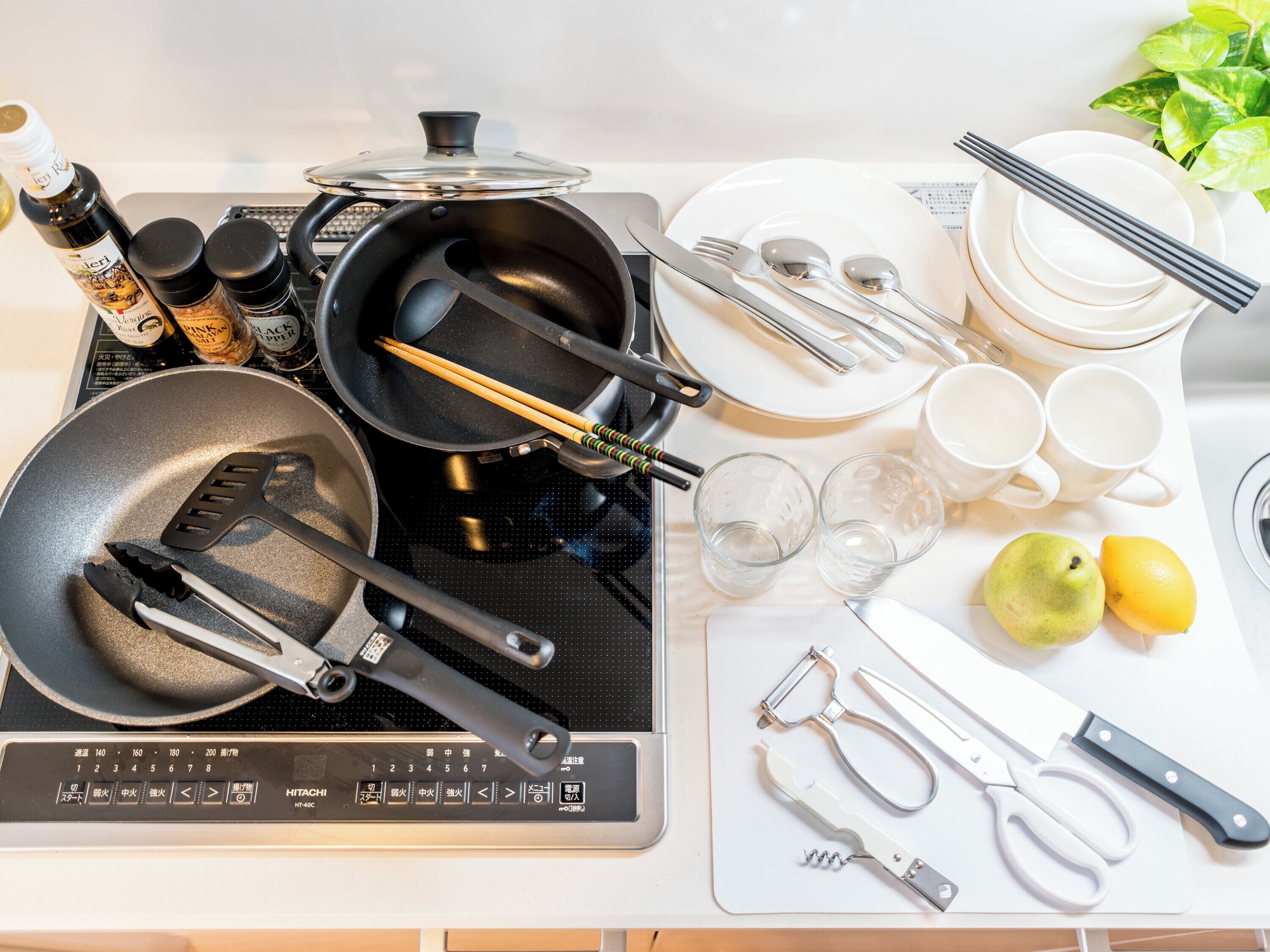 A kitchen with a stove, various cooking utensils, a cutting board, and a fruit bowl.