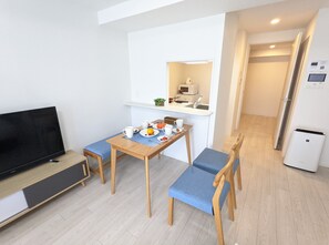 A compact living space with a dining table set for two, a television, a kitchenette, and a refrigerator.