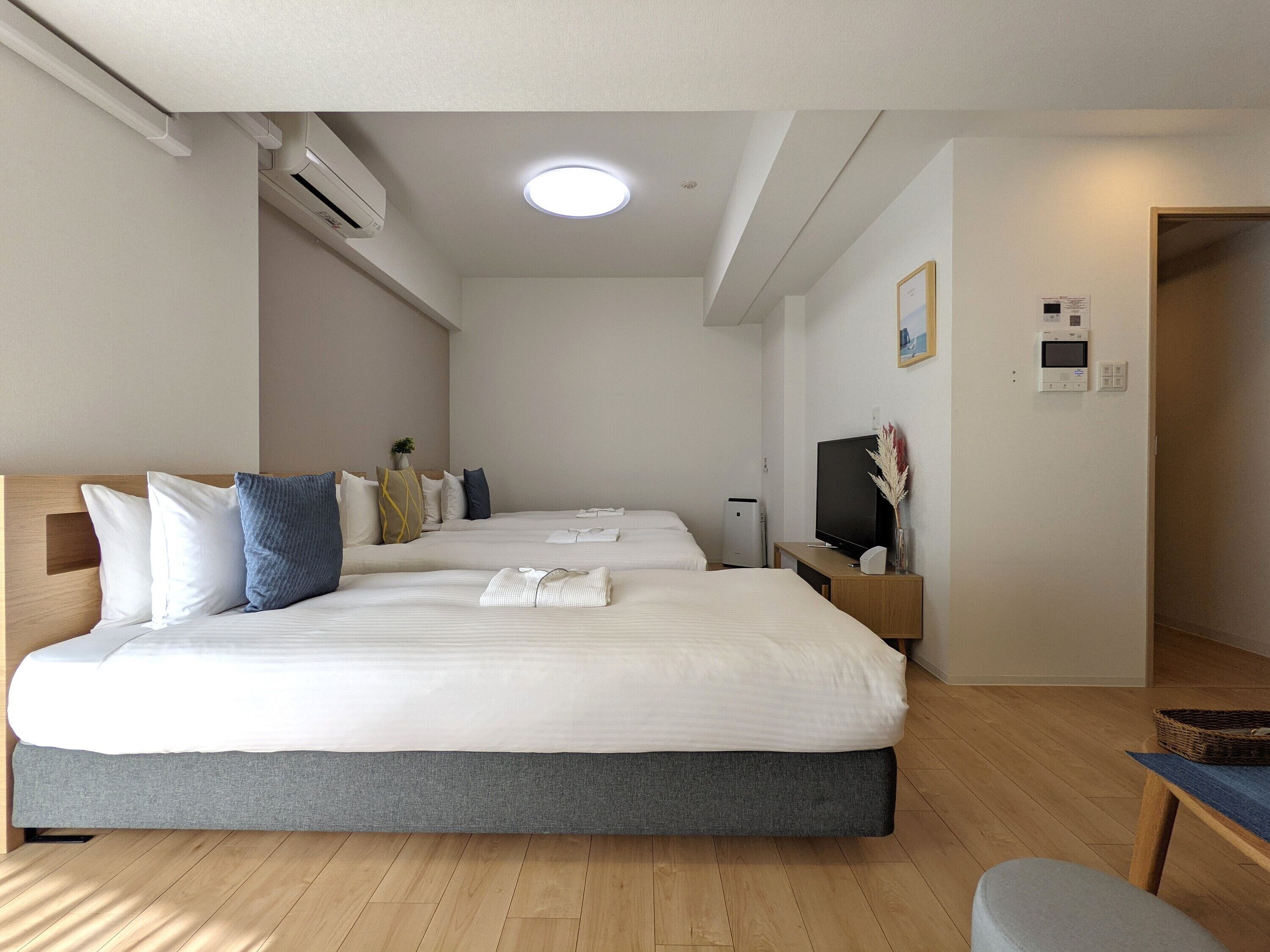 A modern hotel room with two beds, a flat-screen TV, a bedside table, and a small seating area.