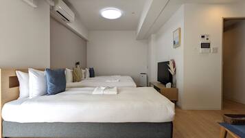 A modern hotel room with two beds, a flat-screen TV, a bedside table, and a small seating area.