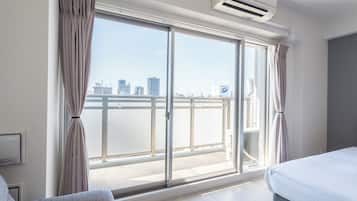 A hotel room with a large sliding glass door to a balcony, a bed, a sofa, and an air conditioning unit.