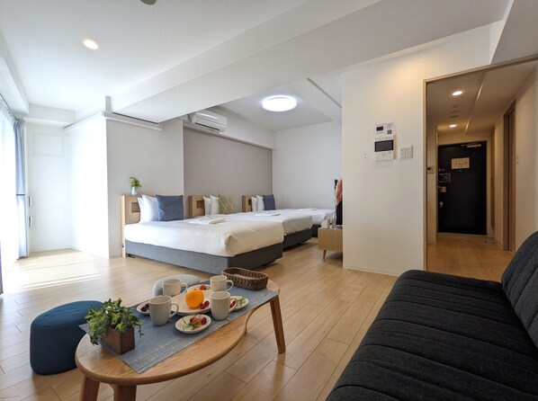 A modern hotel room with a large bed, a sofa, a dining table with fruit and cups, and a small side table. - ESLEAD HOTEL OSAKA TSURUHASHI (Osaka)