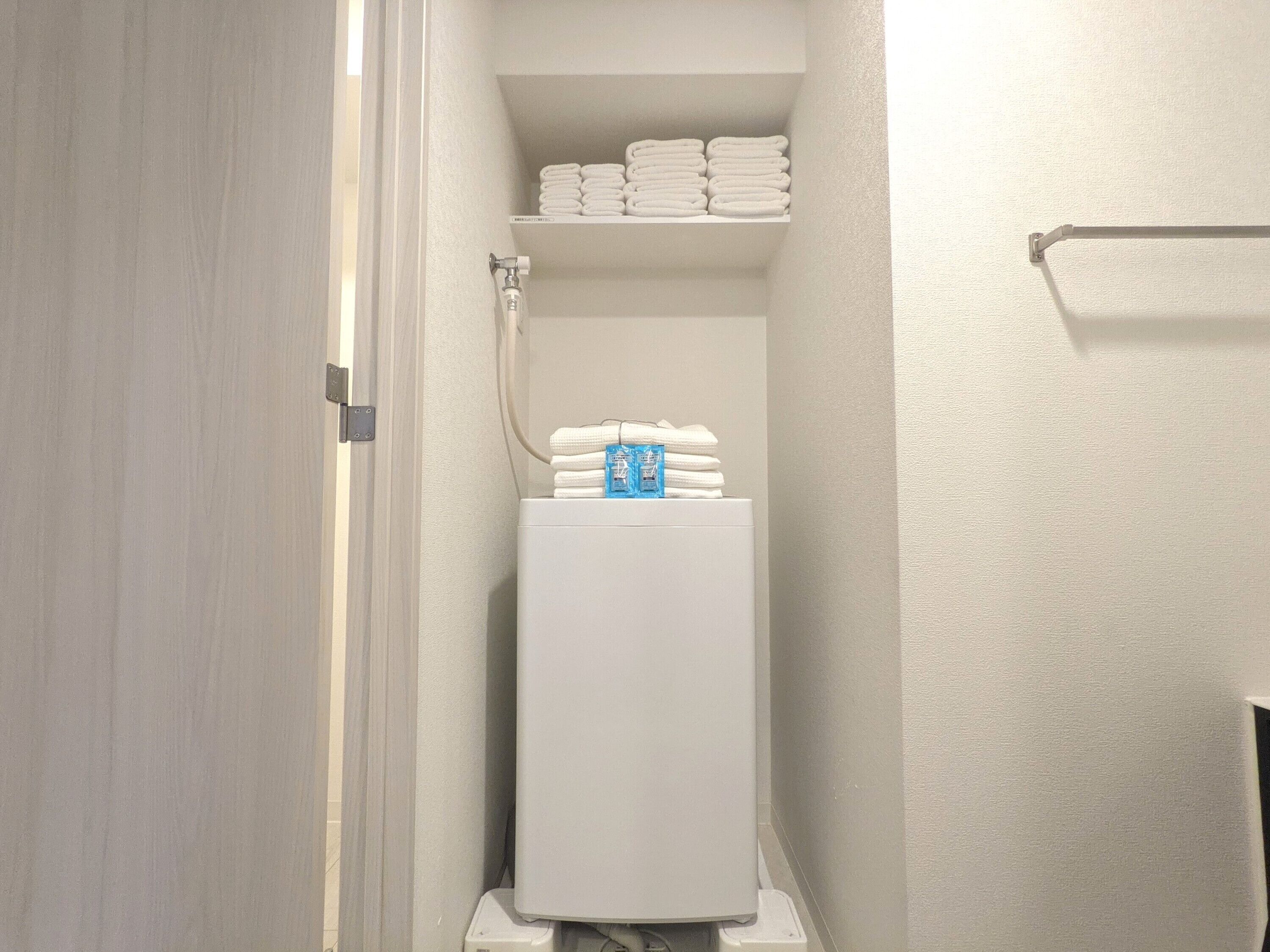 A compact bathroom with a toilet, a towel rack, and a shelf with folded towels.
