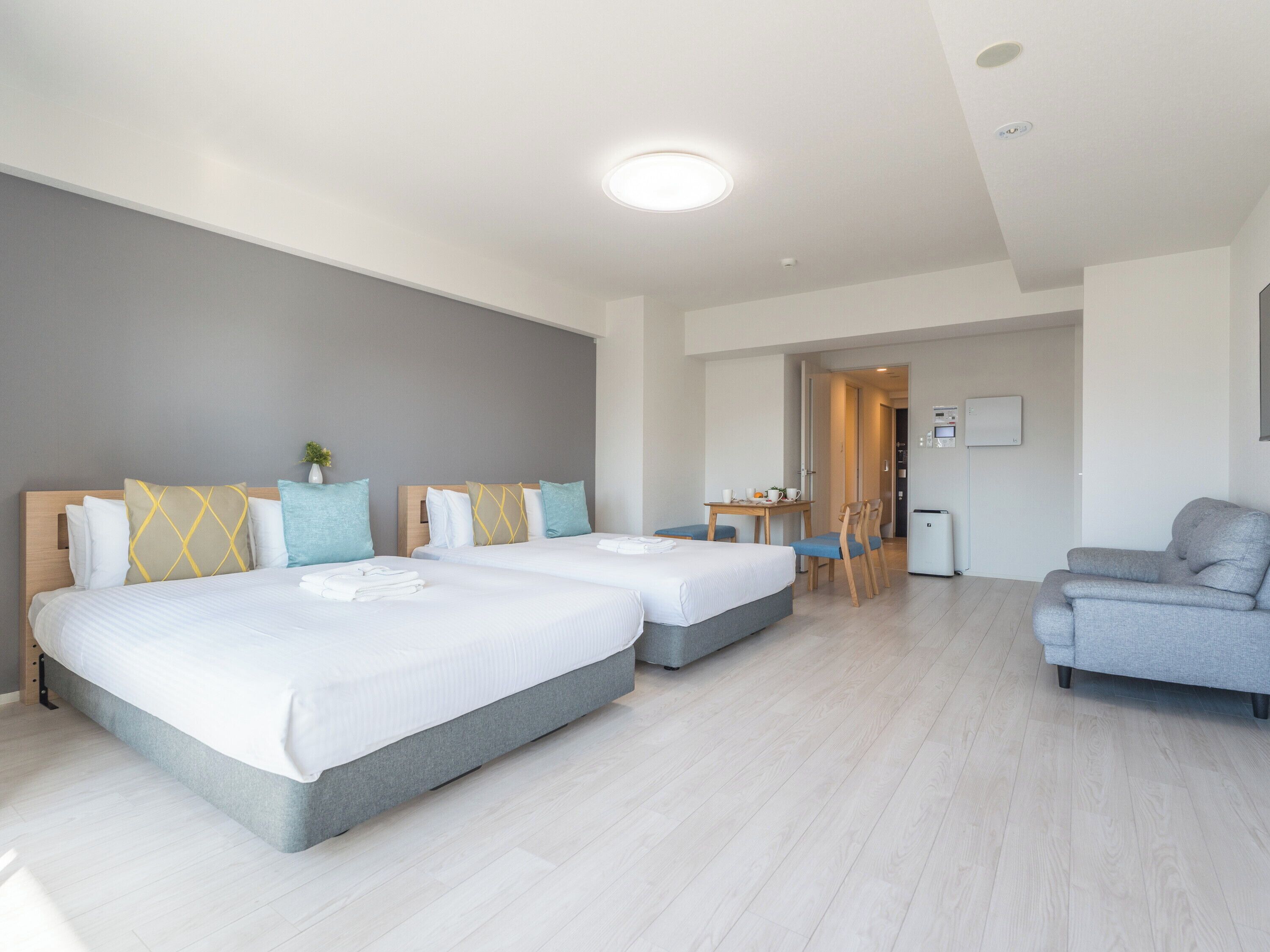 A hotel room with two beds, a desk, a chair, and a sofa.
