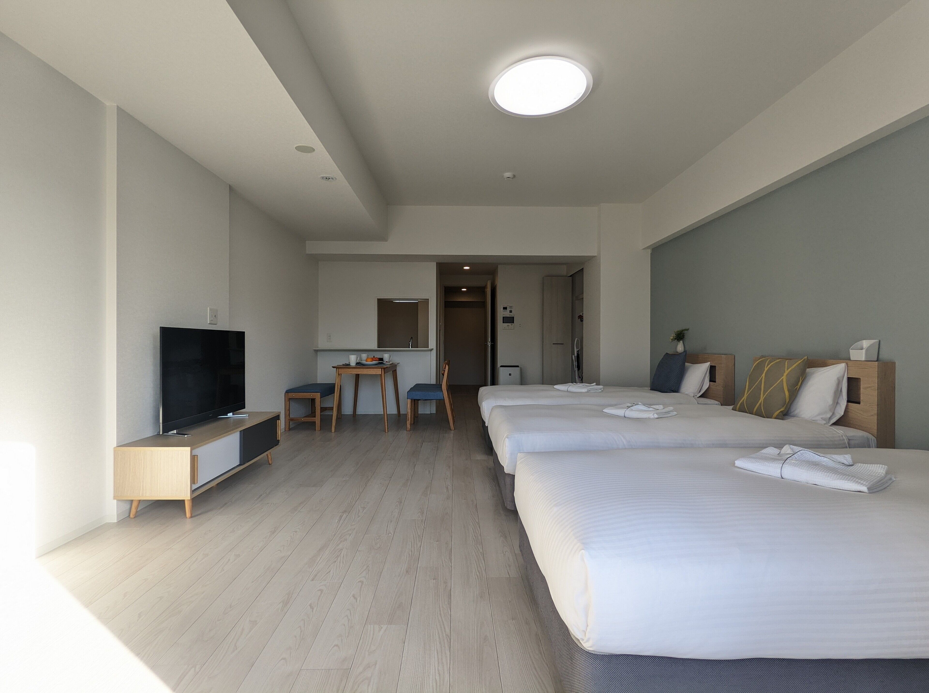 Habitación de hotel con televisor, escritorio, dos sillas, cama con toallas y espejo.