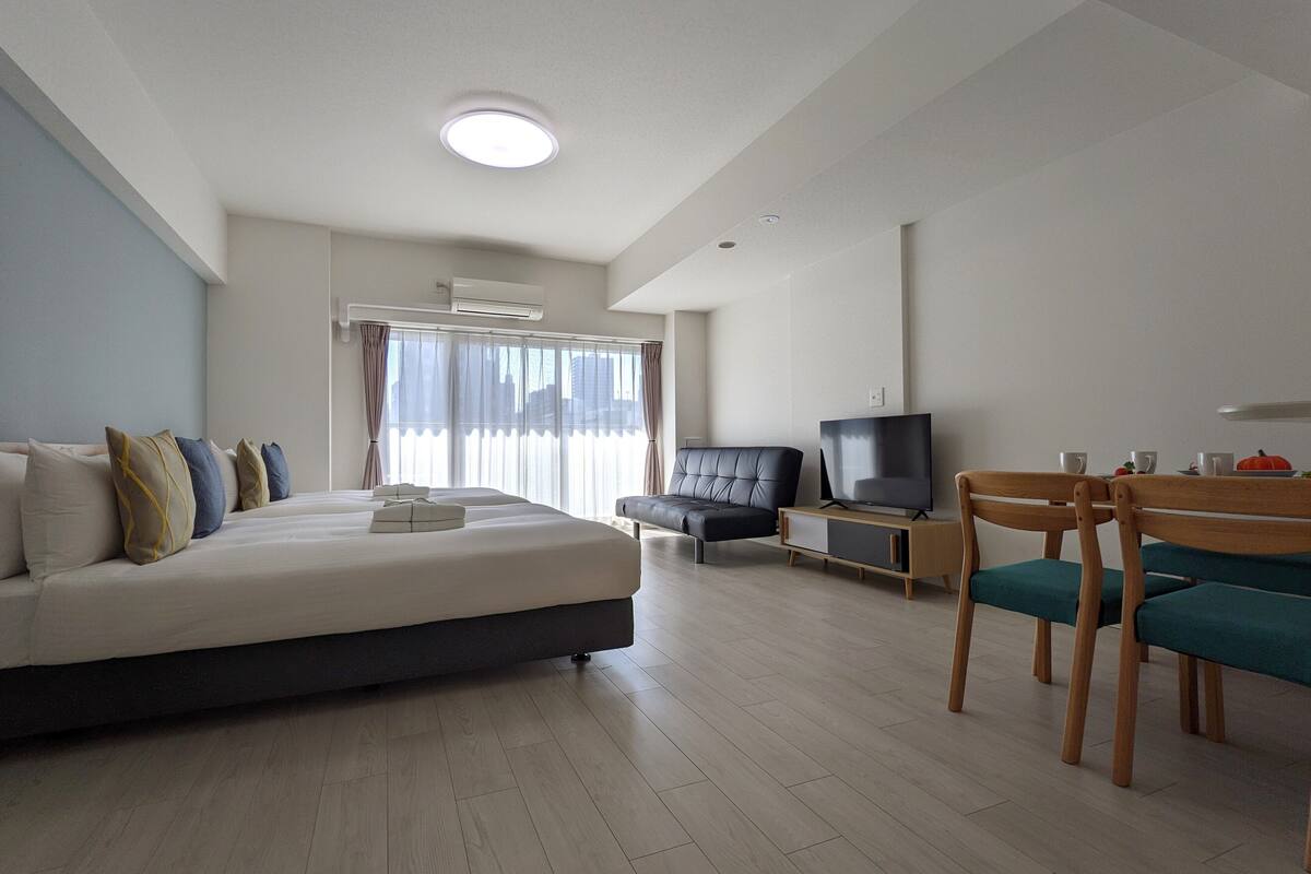 A hotel room with a large bed, a TV, a seating area with chairs, and a window with curtains.