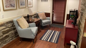 A cozy living room with two armchairs, a coffee table, and a fireplace. There are framed pictures on the wall and a door with a window.