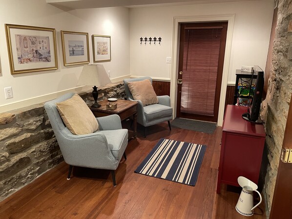 A cozy living room with two armchairs, a coffee table, and a fireplace. There are framed pictures on the wall and a door with a window.