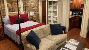 A bedroom with a four-poster bed, a sofa, a coffee table, a wardrobe, and a kitchen area.