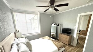 A bedroom with a bed, a ceiling fan, a dresser, a TV, a mirror, and a window with blinds. - Modern Peaceful Pool Home, 25 Mins To Theme Parks! (St. Cloud)