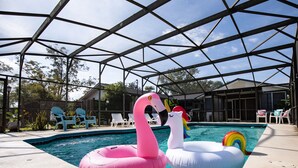 An indoor swimming pool with inflatable swan and unicorn floats, surrounded by lounge chairs and a covered patio area. - Modern Peaceful Pool Home, 25 Mins To Theme Parks! (St. Cloud)