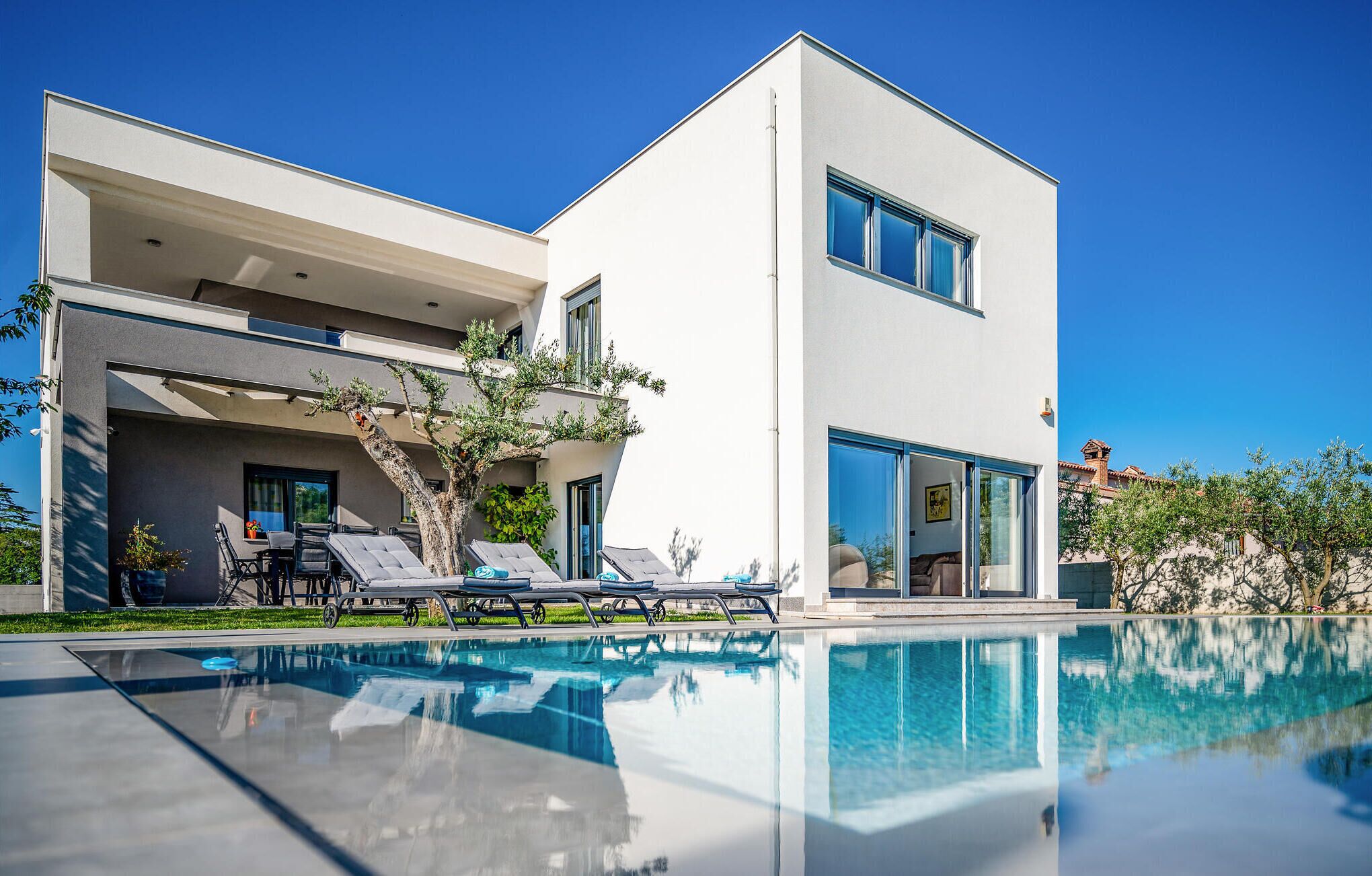 A modern two-story house with a swimming pool, outdoor seating, and a garden.