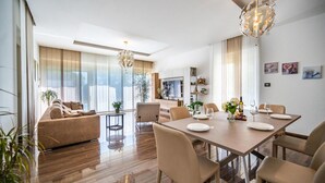 A modern living room with a sofa, dining table, and chairs. There is a TV mounted on the wall and a chandelier hanging from the ceiling. - Beach front home in Pula (Pula)