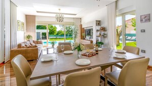 A modern dining area with a large table set for six, surrounded by comfortable seating. A large window offers a view of a swimming pool and greenery. - Beach front home in Pula (Pula)