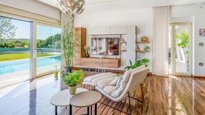 A modern living room with a large TV, a sofa, a coffee table, and a view of a swimming pool. - Beach front home in Pula (Pula)