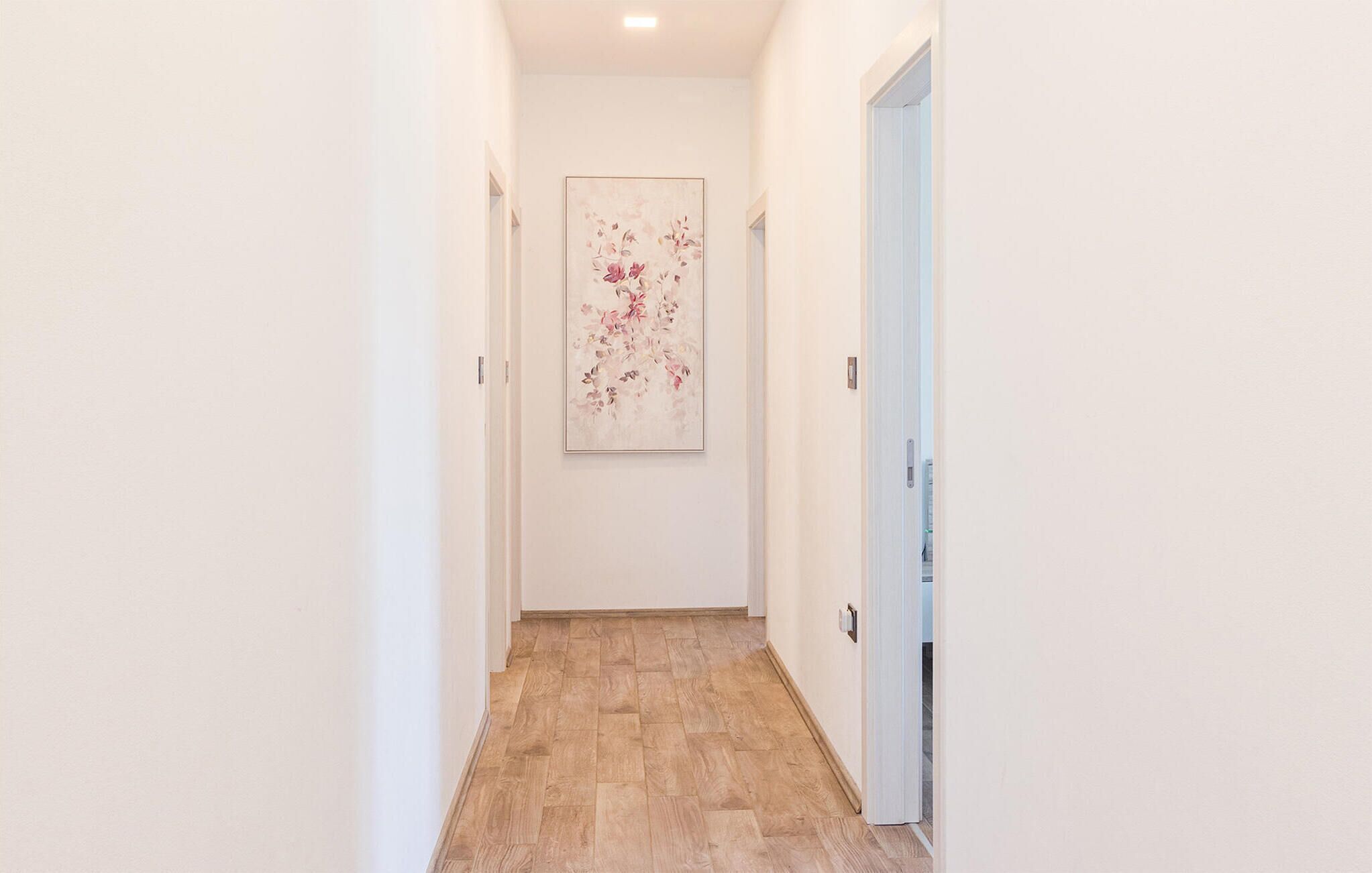 Un couloir étroit doté d’un plancher en bois et orné d’une œuvre d’art florale encadrée au mur.