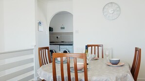 A dining area with a table set for four, surrounded by wooden chairs. A clock is mounted on the wall above the table. - Sunny Side Up Beach House in Tywyn (Tywyn)