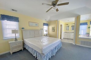 Un dormitorio con una cama grande, un ventilador de techo, una ventana con persianas, una mesita de noche y un aparador.