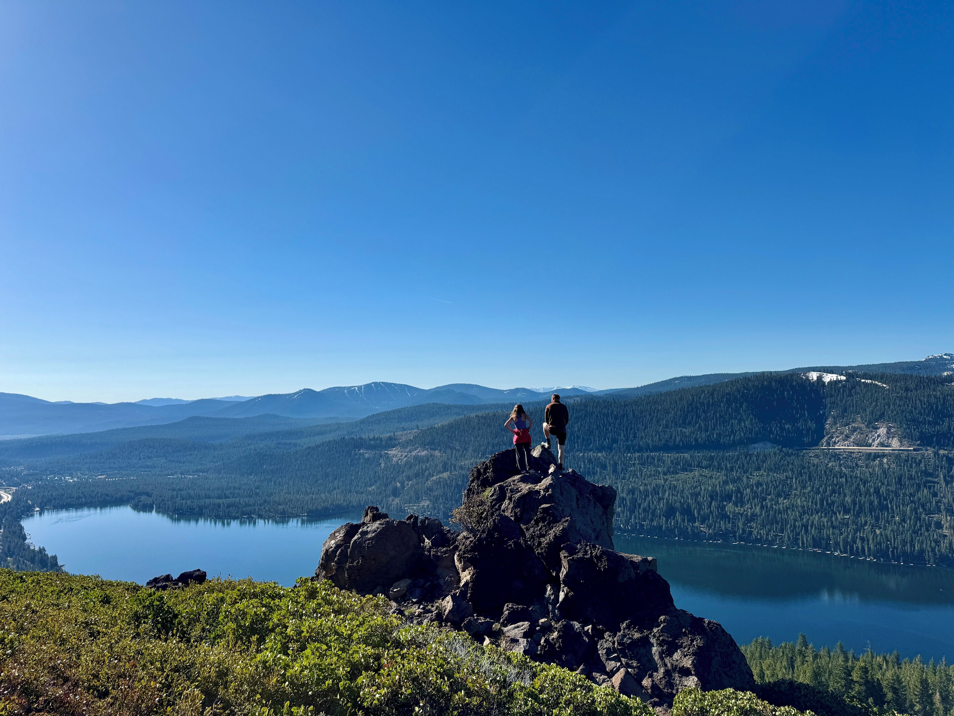 Un paisaje montañoso con un lago, bosque y afloramiento rocoso.