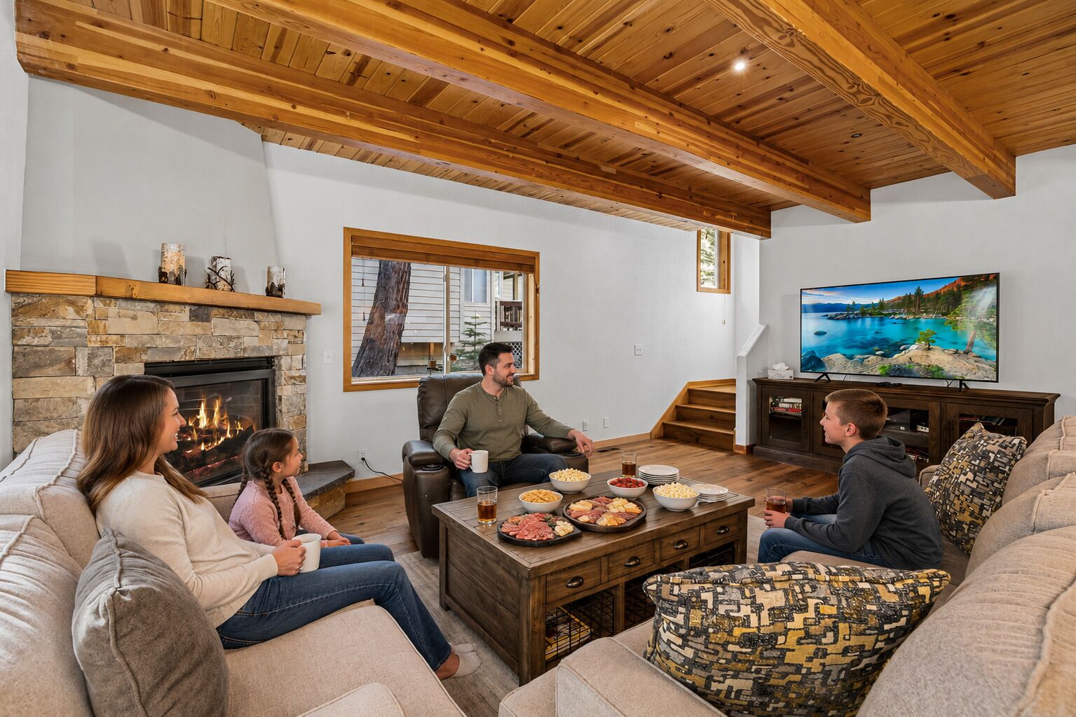 Ein gemütliches Wohnzimmer mit Kamin aus Stein, Holzbalkendecke, Fernseher und einem Esstisch mit Speisen.