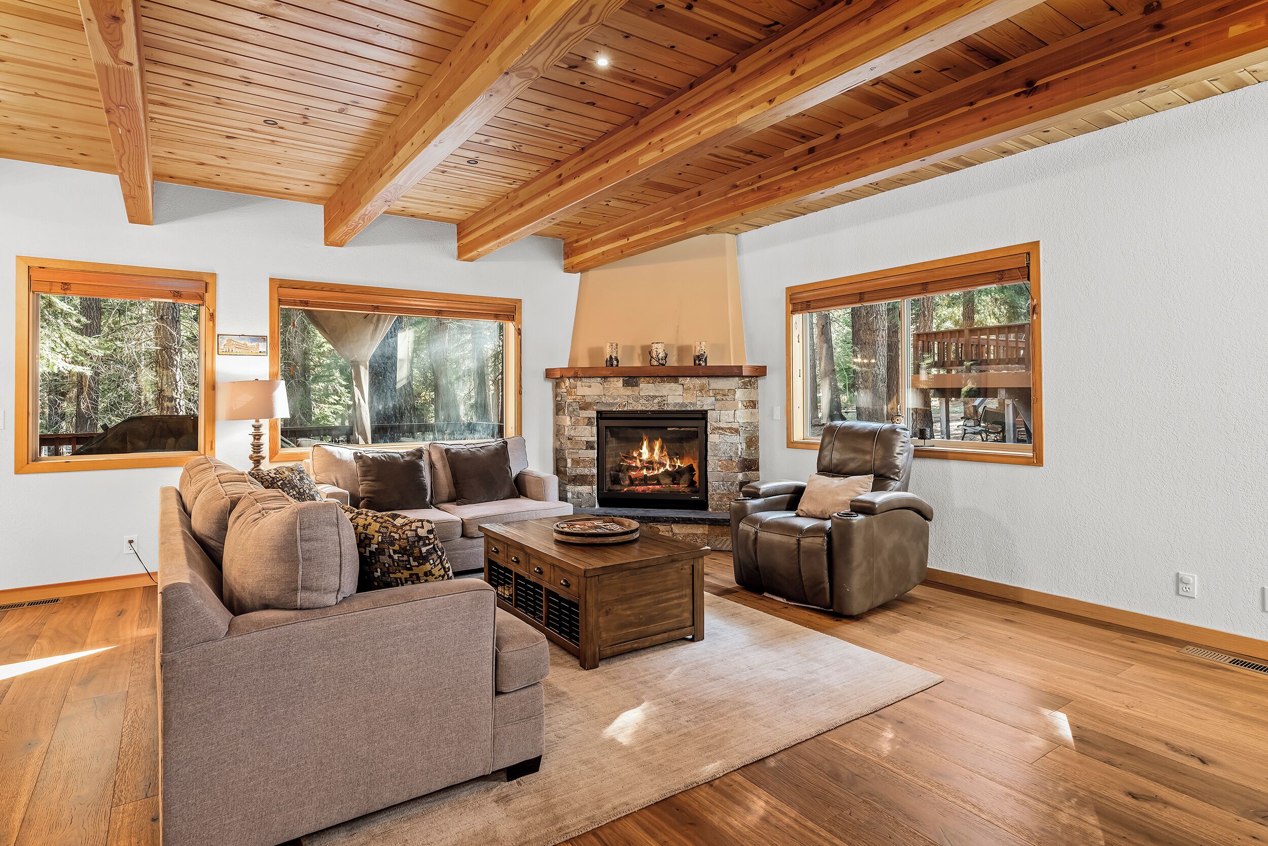 A spacious living room with a fireplace, wooden ceiling beams, large windows, and a cozy seating area.