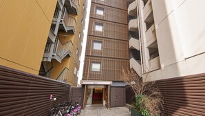 A narrow alleyway between two buildings with balconies, a sign for 'Rokuten Stay,' and a small garden area.