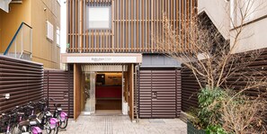 Un edificio con un letrero que dice 'Rakuten STAY URBAN', una entrada con rejas y bicicletas estacionadas afuera.