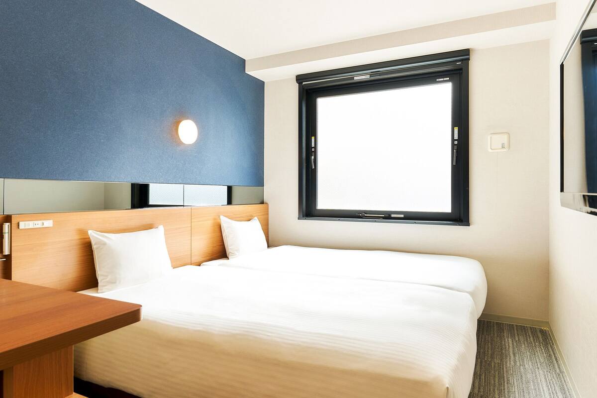 Una habitación de hotel con cama, un escritorio de madera, una ventana y un televisor instalado en la pared.
