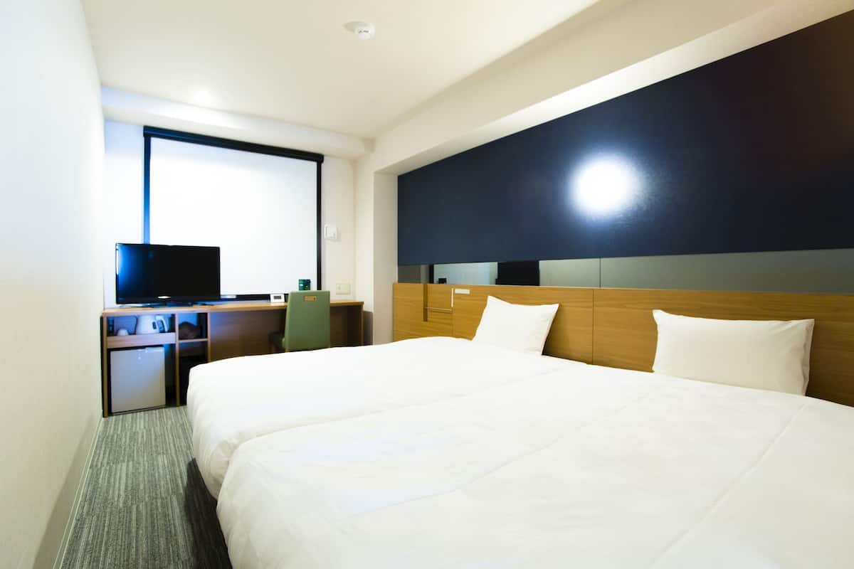 Quarto de hotel com uma cama grande, uma escrivaninha com computador e uma televisão.