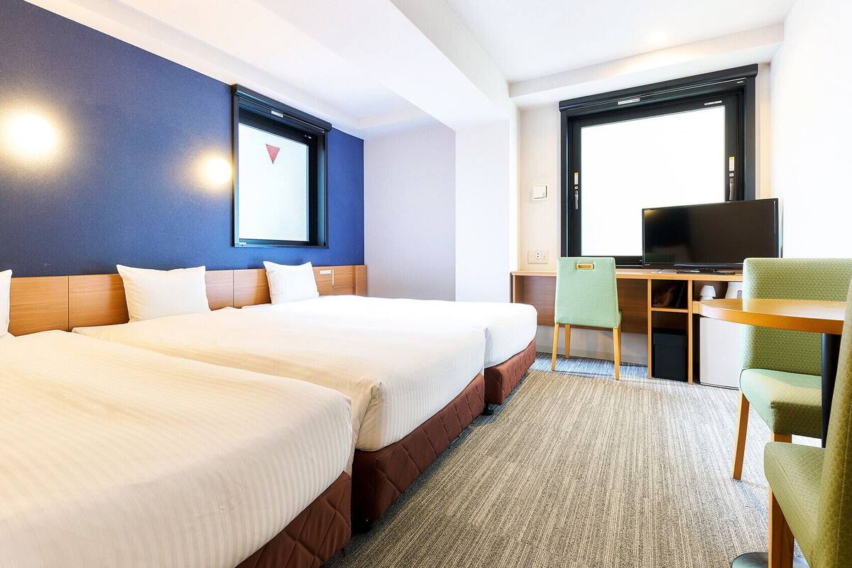 Hotellihuone, jossa on kaksi sänkyä, työpöytä tuolilla, televisio ja ikkuna.
