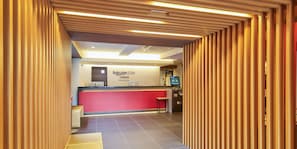 Zona de recepción con un mostrador rojo, una pantalla digital y un panel de madera.