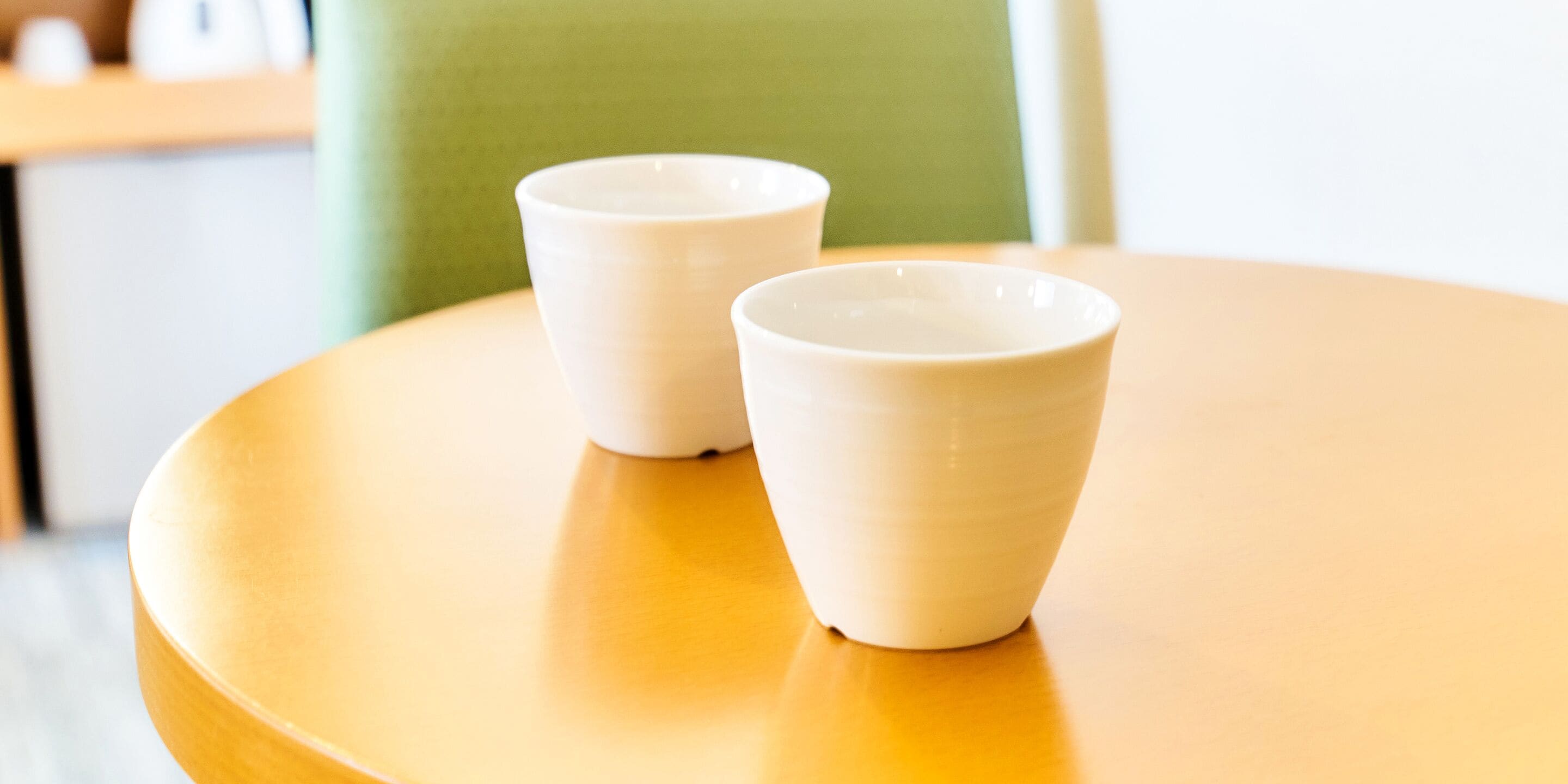 Two white ceramic cups on a round wooden table.