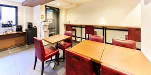 Un comedor con sillas tapizadas rojas y una mesa de madera, una cafetera y un refrigerador.