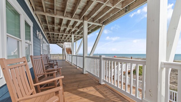 A wooden deck with white railings, wooden chairs, and a view of the ocean. - "Happily Ever After" Luxury Oceanfront home w/ Private Pool, 10 Bedrooms, 10.5 Baths (Holden Beach)