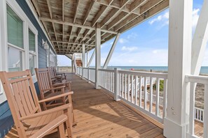 A wooden deck with white railings, wooden chairs, and a view of the ocean. - "Happily Ever After" Luxury Oceanfront home w/ Private Pool, 10 Bedrooms, 10.5 Baths (Holden Beach)