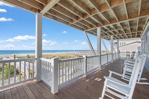 Enjoy the serene ocean views from this expansive deck, featuring comfortable rocking chairs and a picturesque beach scene.