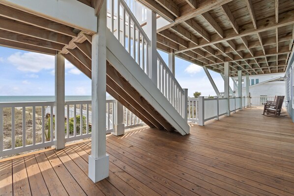 Une terrasse en bois avec un escalier menant à un niveau supérieur, d’où l’on a vue sur une plage.