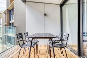 Un balcone con tavolo e sedie in legno, una lampada a sospensione e ringhiera in vetro.