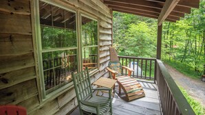 Una baita di legno con veranda, ampie finestre e vista sulla foresta.