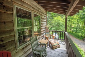 Relax on the porch with two Adirondack chairs and a small table, taking in the view of the surrounding forest from the large windows.