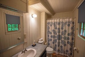 Et badeværelse med træbeklædning, en vask, toilet og et bruseforhæng med blomstermønster.