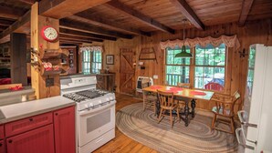 L'interno di un rifugio rustico con una cucina, una stufa, un tavolo da pranzo con sedie e un'ampia porta di legno.