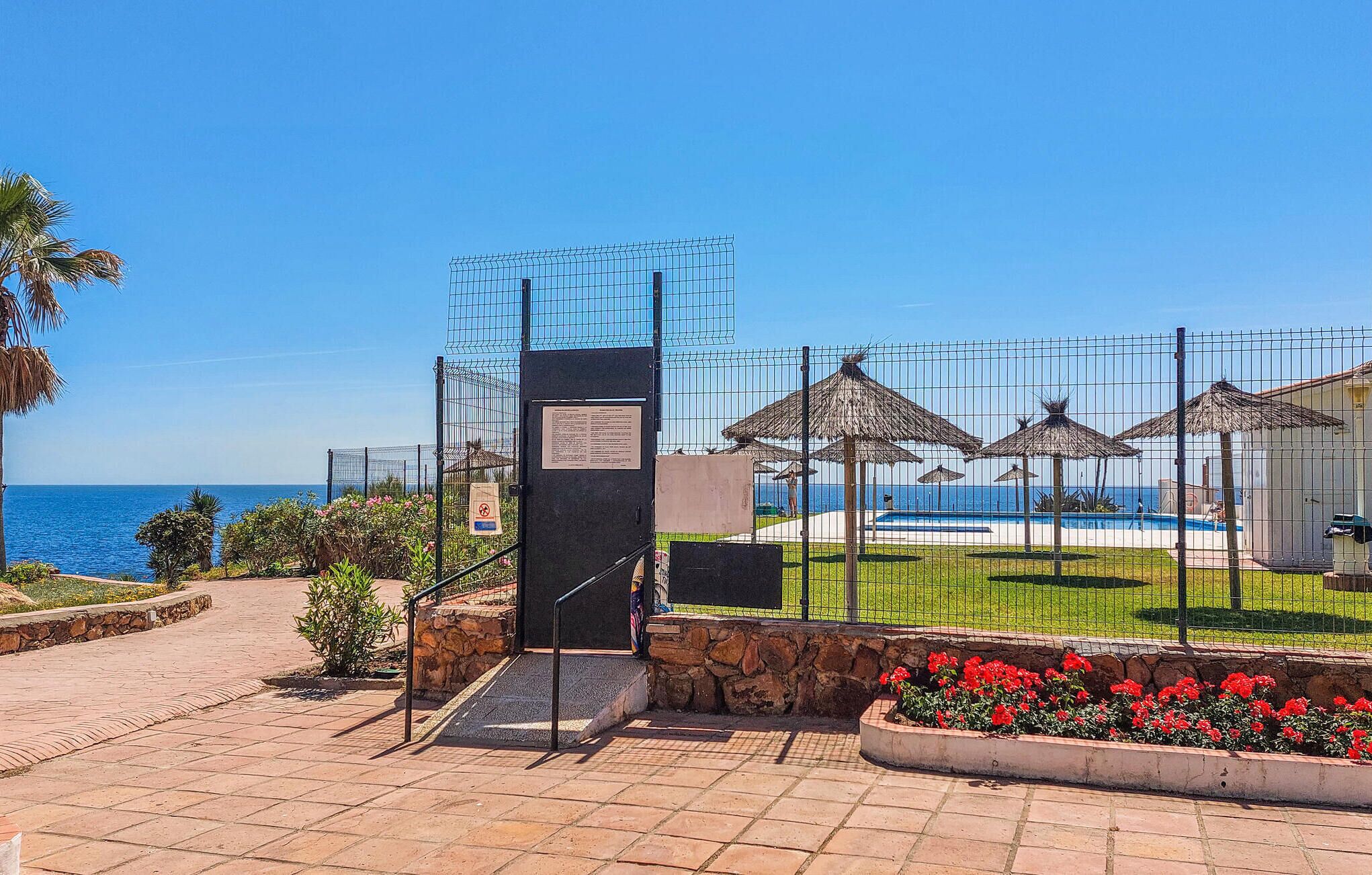 A gated entrance with a sign, a swimming pool, and beach umbrellas.