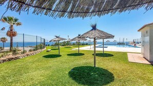 Un espace piscine agrémenté de parasols en chaume, offrant une vue dégagée sur la mer et doté d’une pelouse bien entretenue.