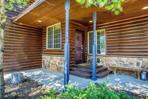 A log cabin with a stone foundation, wooden exterior, and a porch with steps leading to a door.