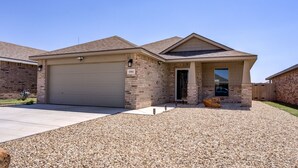 A two-story house with a garage, a covered entryway, and a gravel driveway. - Milano Guesthouse (Lubbock)