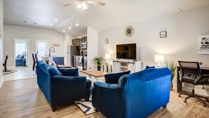 A modern living room with a ceiling fan, a TV, and a dining area with a table and chairs. - Milano Guesthouse (Lubbock)
