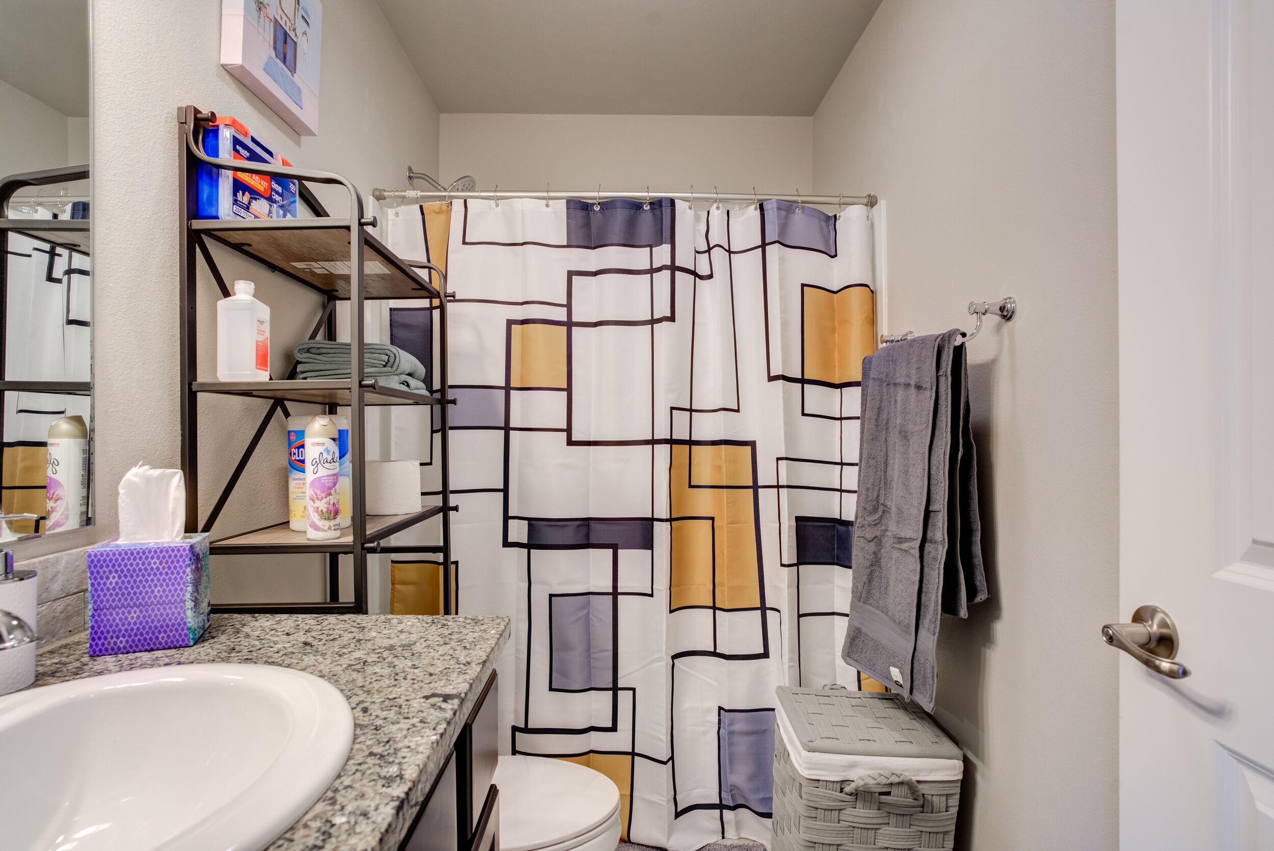 A bathroom with a shower curtain, a sink, a toilet, and a towel rack.